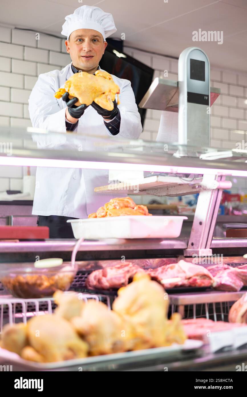 Macellaio maschile che mostra pollo intero fresco in macelleria Foto Stock