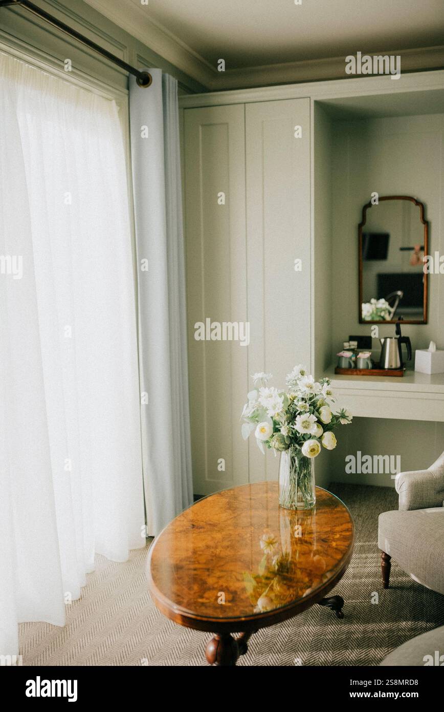 Una stanza con un tavolo di legno e un vaso di fiori. La camera è ben illuminata e ha un aspetto pulito e minimalista Foto Stock