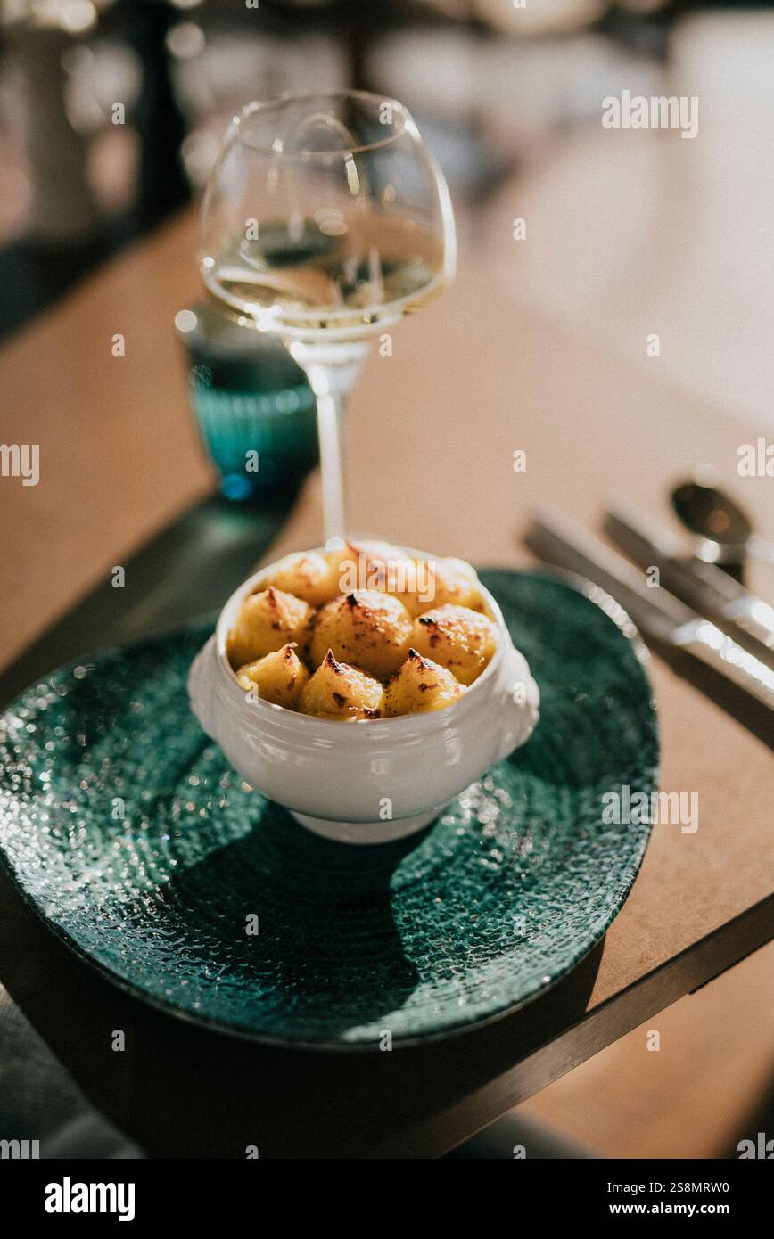 Una ciotola di cibo con un bicchiere di vino su un tavolo. La ciotola è piena di piccole patate dorate e il bicchiere di vino è pieno a metà. La scena è rilassata e io Foto Stock