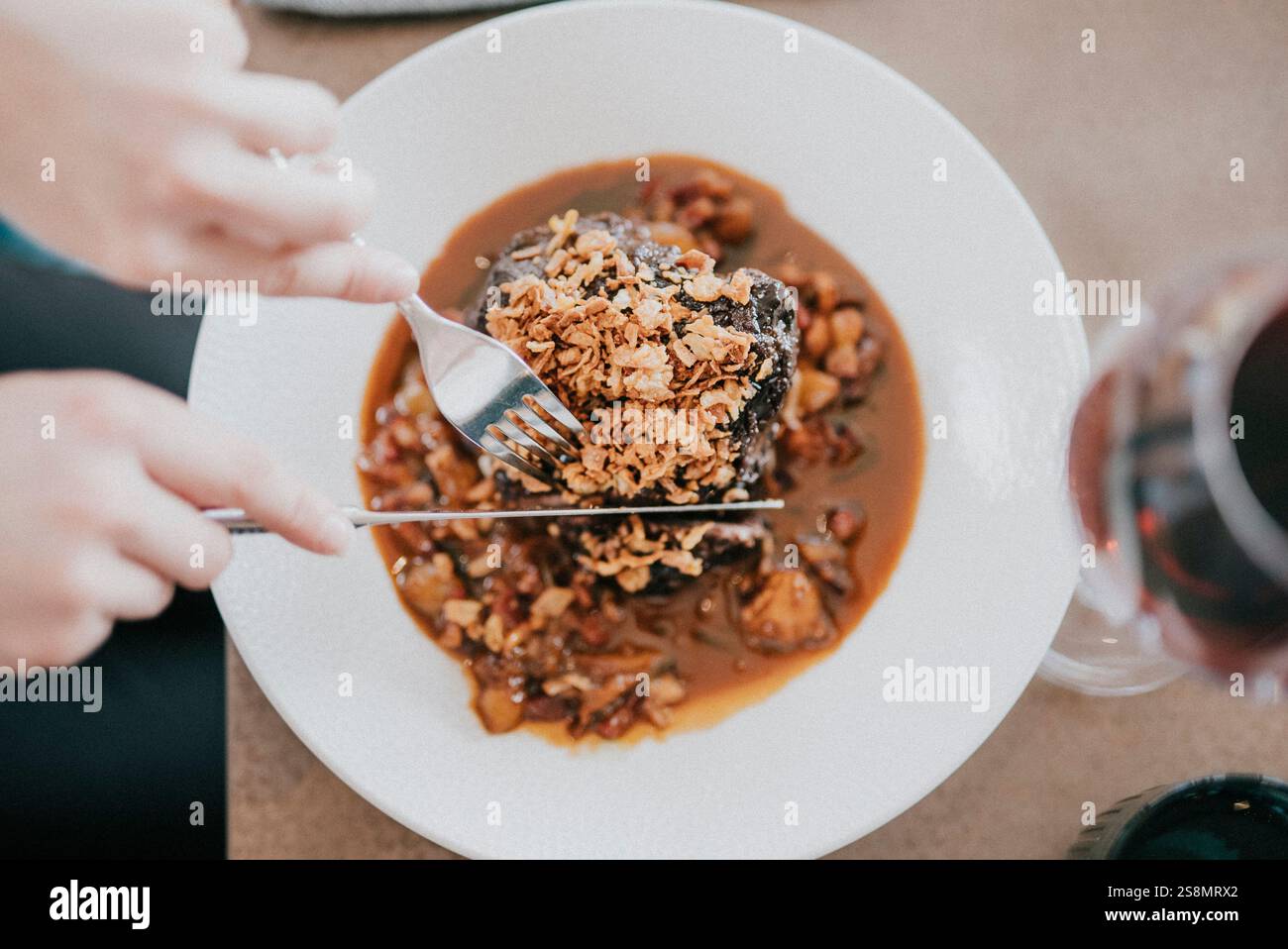 Una persona sta mangiando un pasto con una forchetta e un coltello. Il pasto consiste in un pezzo di carne e un lato di riso. La persona tiene dentro la forca e il coltello Foto Stock