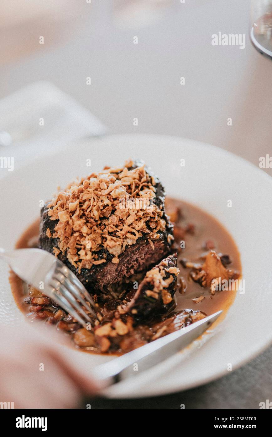 Un piatto di cibo con una forchetta e un coltello. Il cibo è un piatto di manzo con un lato di patate. Il piatto è bianco e il cibo è marrone Foto Stock