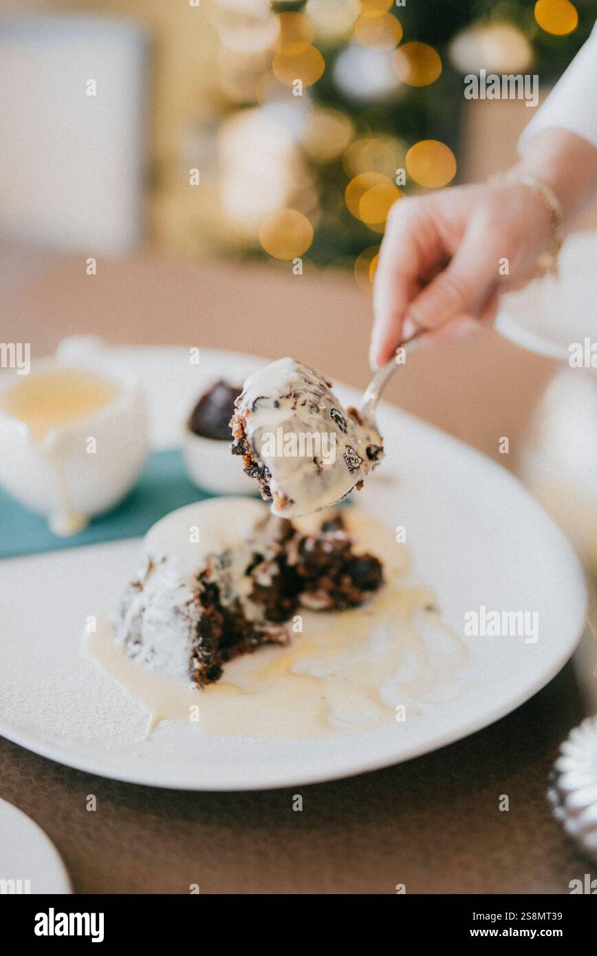 Una persona sta tenendo una forchetta e un cucchiaio sopra un dessert. Il dessert è una torta con un condimento di panna Foto Stock