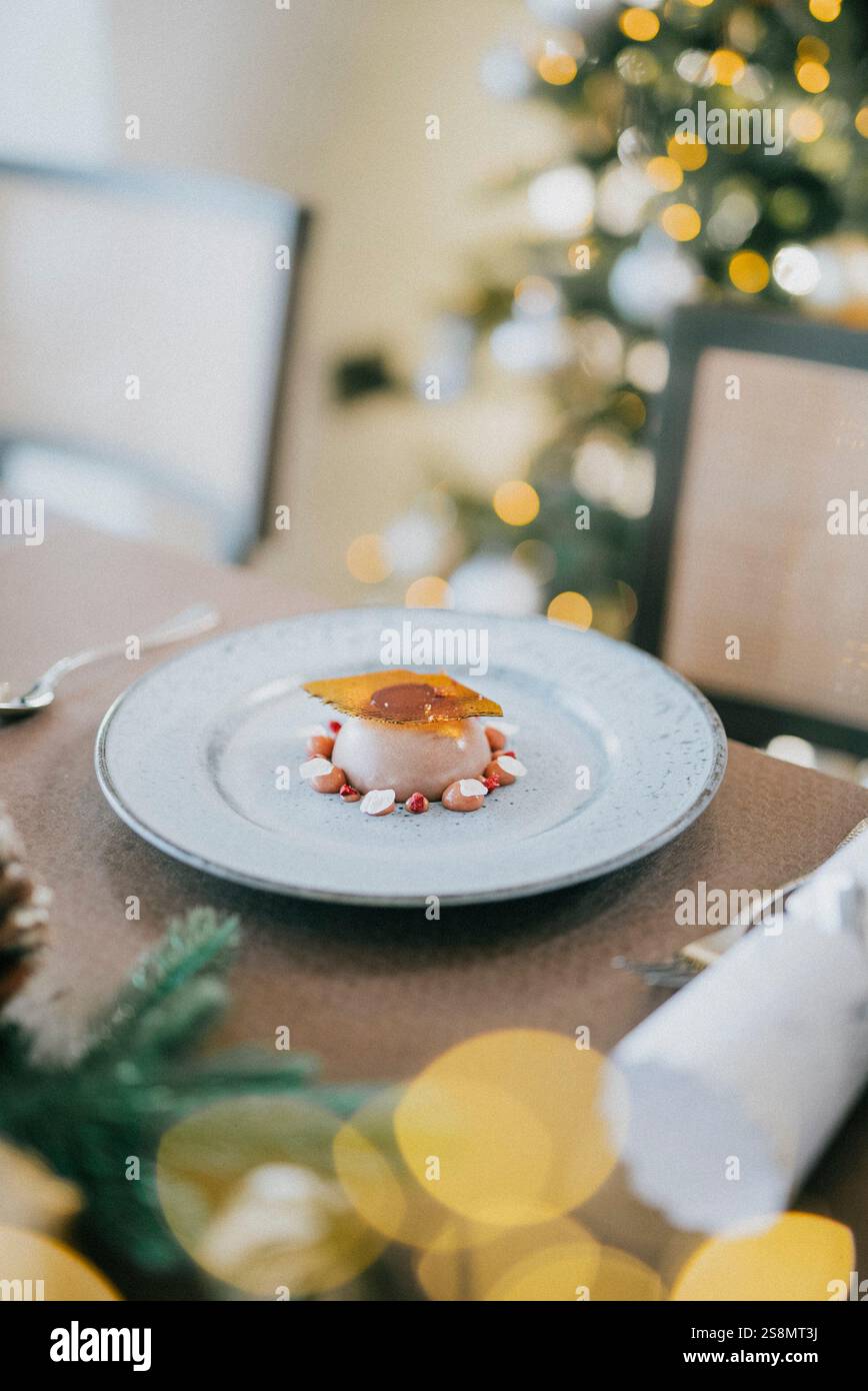 Un dessert è su un piatto davanti a un albero di Natale. Il dessert è una torta con un condimento al caramello Foto Stock