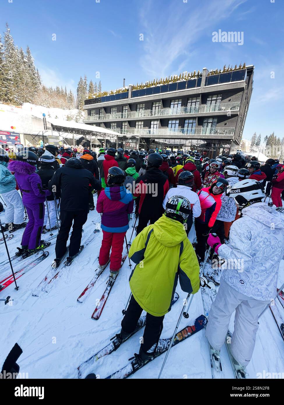 Bukovel, Ucraina - 23 gennaio 2025: Gli sciatori in abiti colorati attendono in una stazione sciistica accanto a un grande edificio, godendosi il sole. La sce Foto Stock