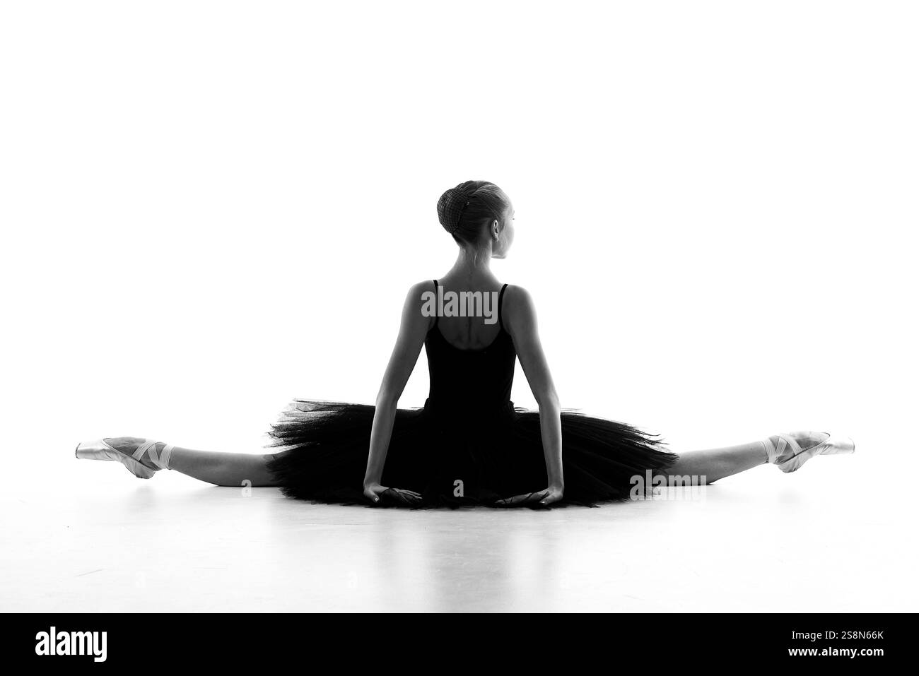 Una ballerina professionale in tutu nero esegue un allungamento del pavimento con leggerezza e grazia, catturato come un'artistica silhouette in bianco e nero. Foto Stock