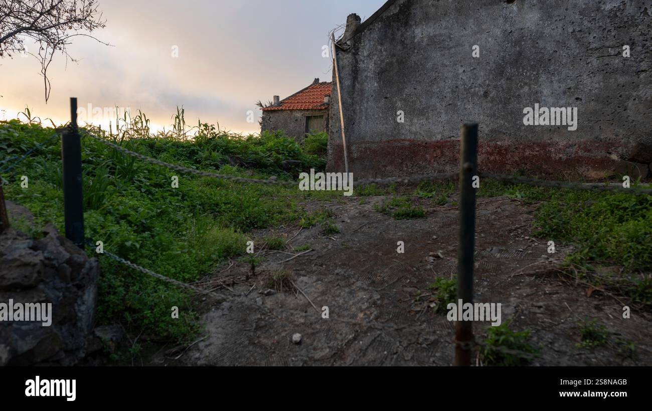 Un appezzamento rurale sovrastato con un muro intemprato e un'area parzialmente recintata. Il sole che tramonta diffonde una calda luce sulla vegetazione e sulla struttura rustica Foto Stock