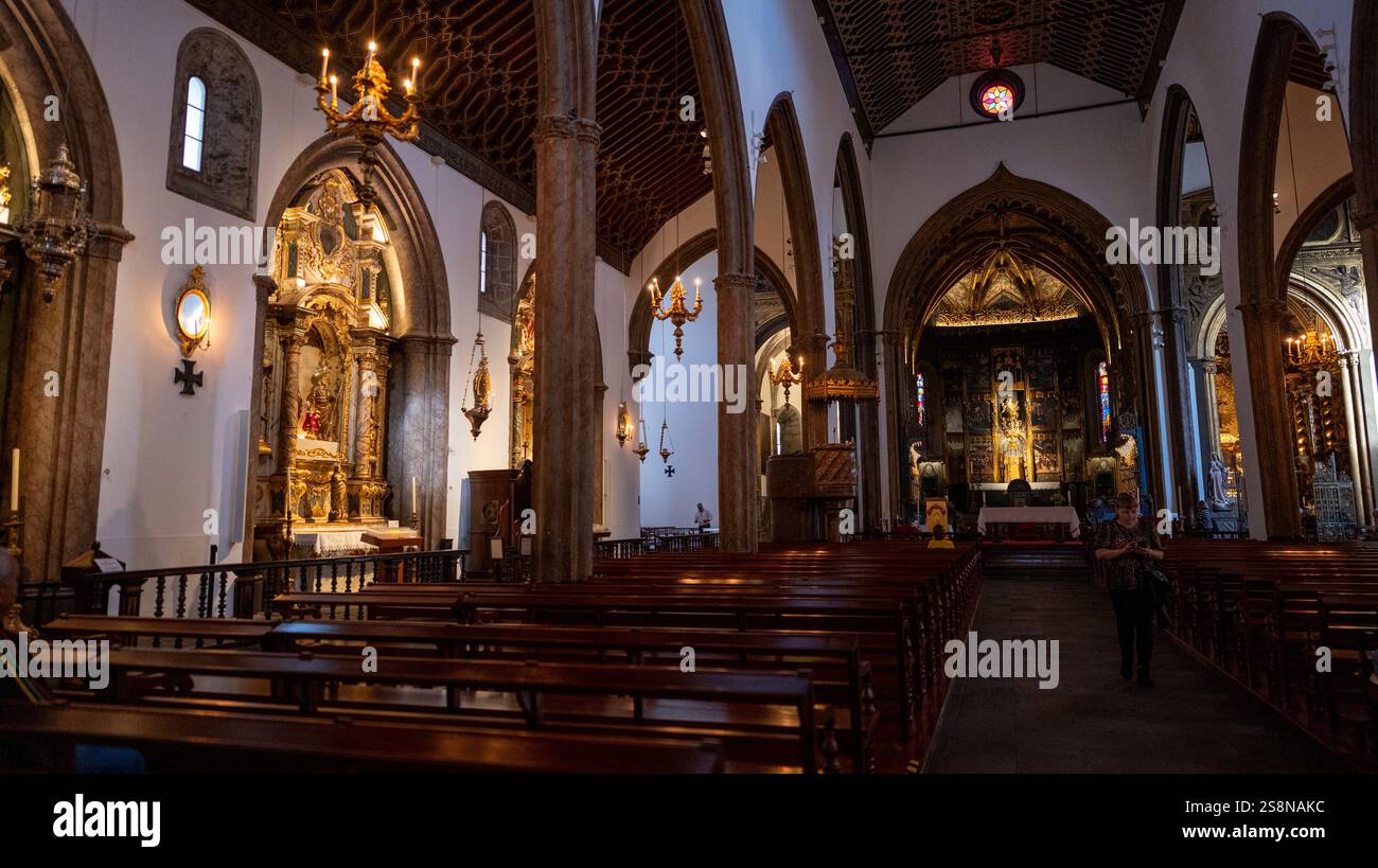 L'interno di una chiesa storica con pali di legno, altari ornati e archi gotici. Una calda illuminazione mette in risalto le dettagliate opere d'arte religiose e i grandi archi Foto Stock