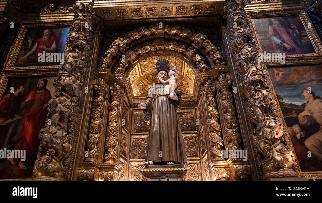 Un altare della chiesa riccamente decorato con una statua di un santo che tiene in braccio un bambino, circondato da intricate incisioni dorate e dipinti religiosi incorniciati. Foto Stock