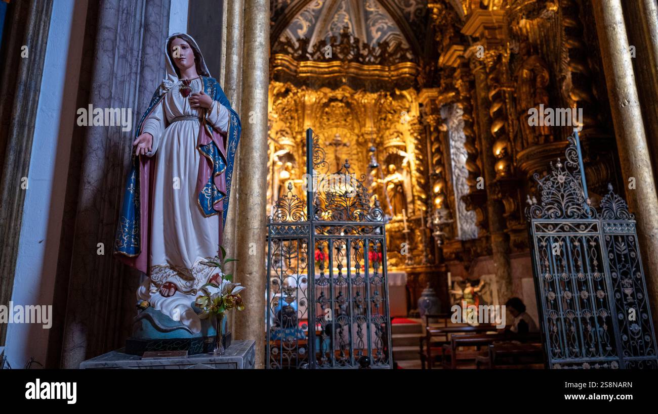 Una statua della Vergine Maria che regge un cuore si trova vicino a un altare dorato ornato, circondato da intricate porte di metallo e da una calda illuminazione interna in un alto Foto Stock