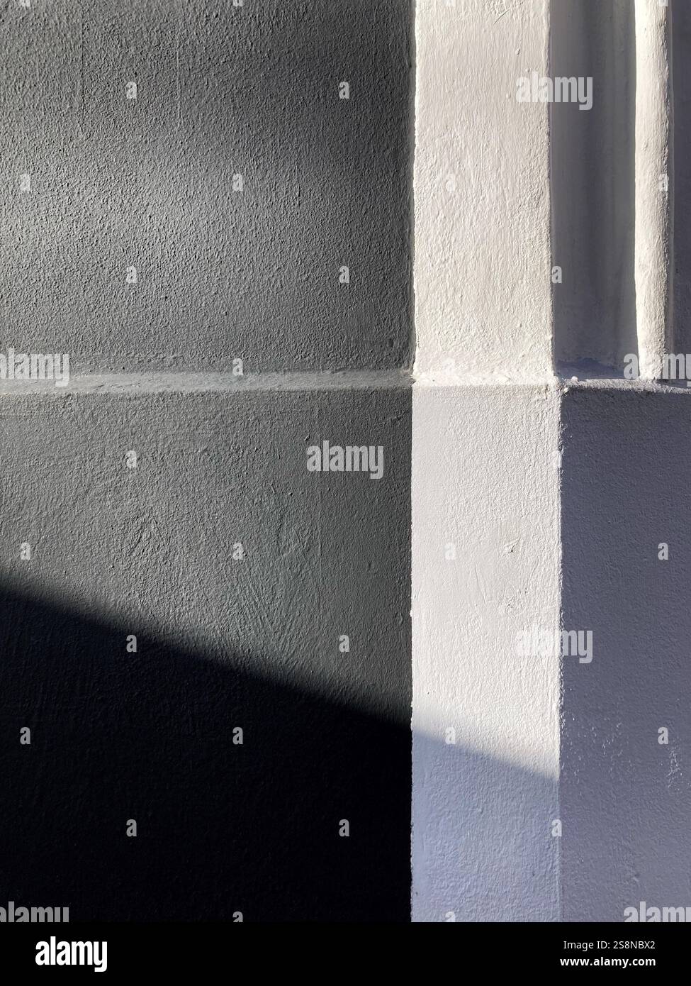 Angolo minimalista di una parete con forti contrasti e ombre, creando una rappresentazione artistica e astratta della luce e della geometria. - Immagine stock catturata con smartphone