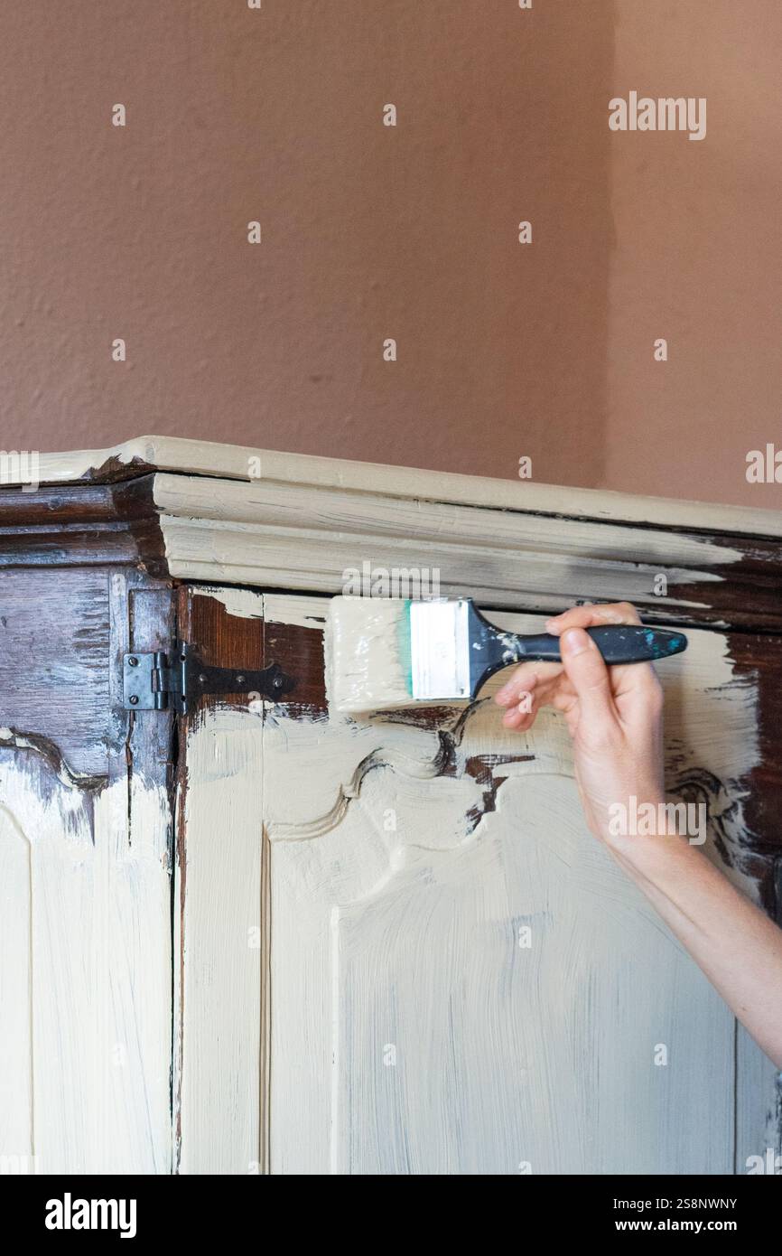 Artigiano che applica vernice di gesso bianco su mobili in legno antico utilizzando pennelli, ristrutturazioni domestiche e concetto di restauro di mobili Foto Stock