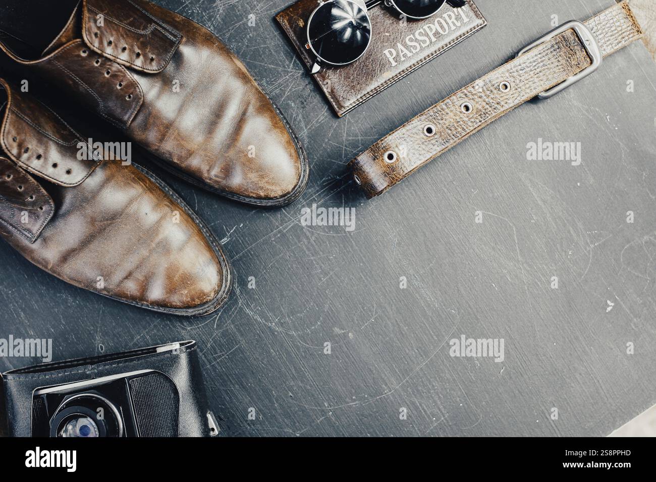 Scarpe marrone, una fotocamera vintage e gli indispensabili da viaggio su una superficie dai toni scuri Foto Stock