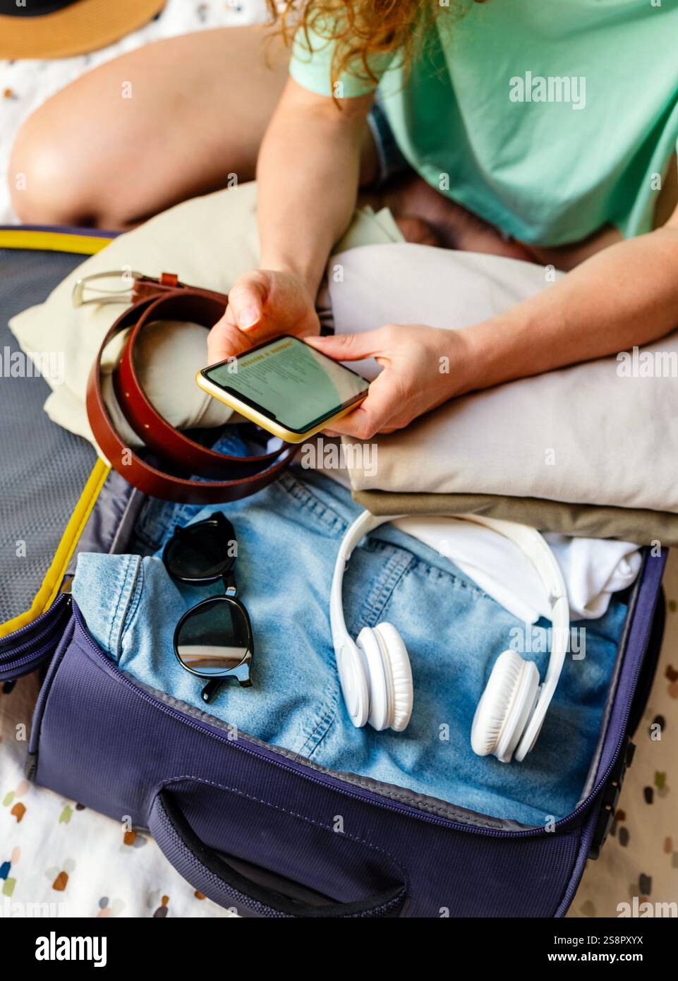 Donna che sta imballando una valigia mentre guarda la sua lista di imballaggio sul suo cellulare Foto Stock