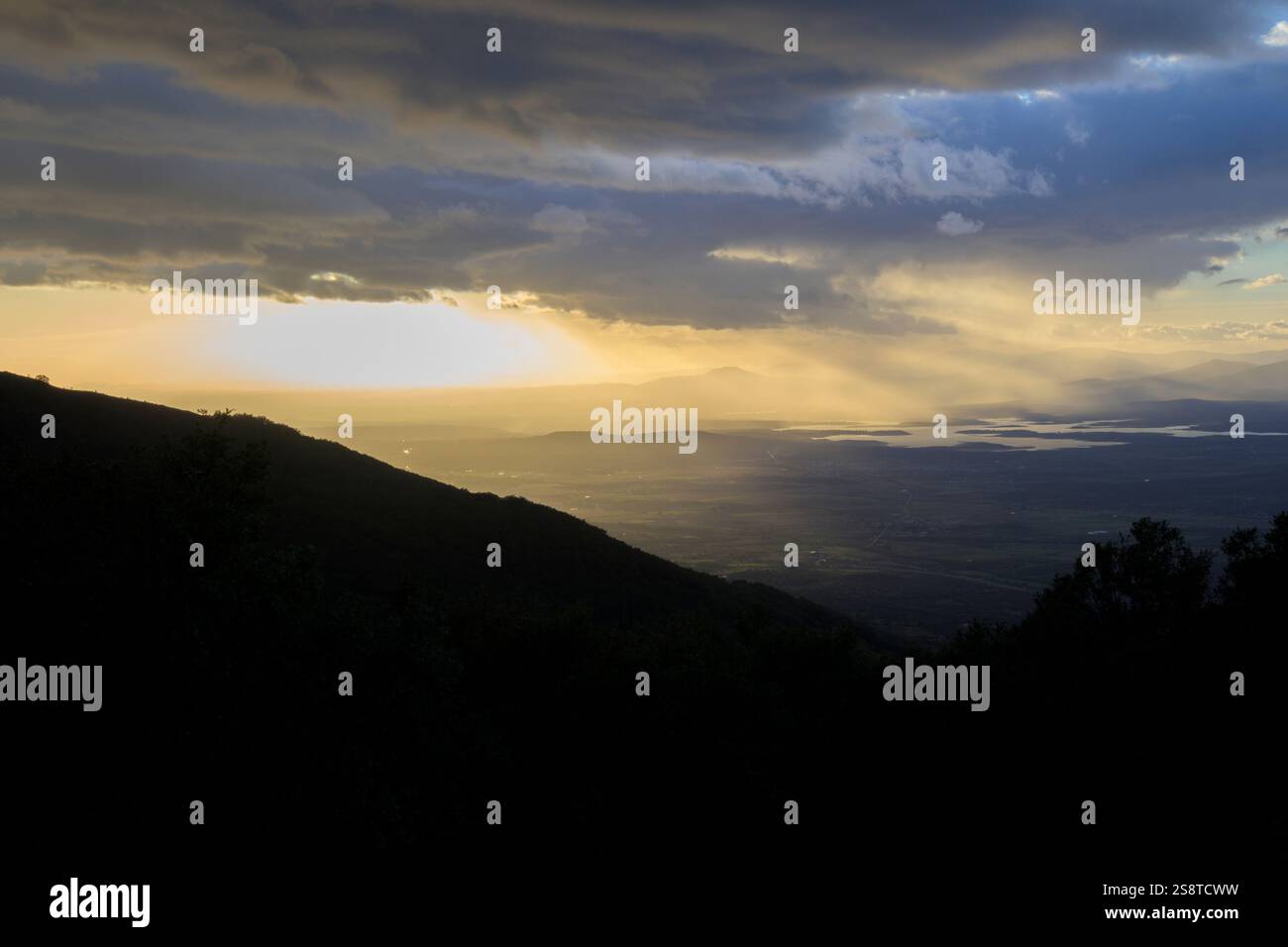 Ultimi raggi di sole all'orizzonte nella valle dalla montagna in una giornata nuvolosa con nuvole orizzontali Foto Stock Ultimi raggi di sole all'orizzonte nella valle dalla montagna in una giornata nuvolosa con nuvole orizzontali Foto Stock