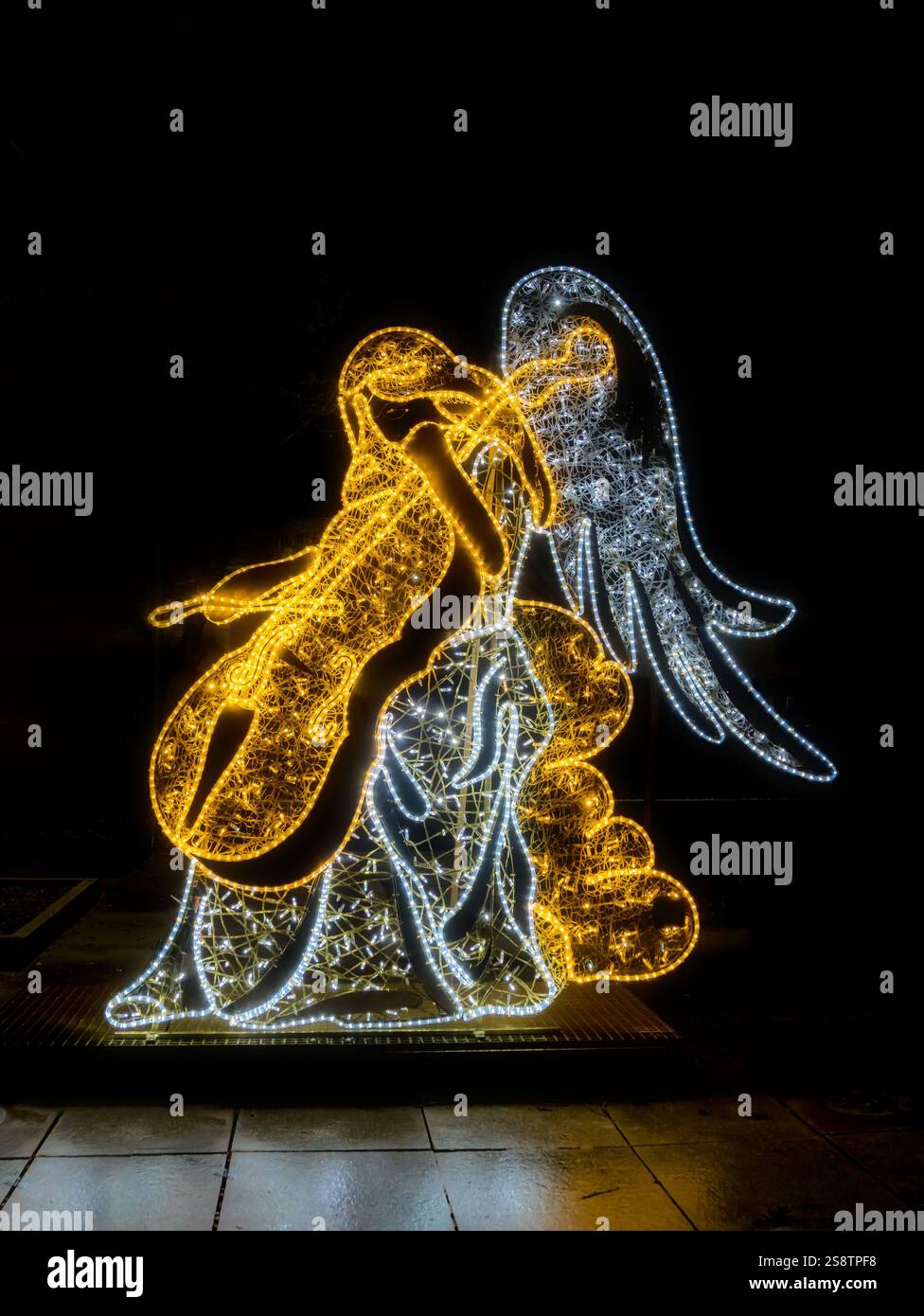 Una scultura d'angelo illuminata splendidamente realizzata che tiene in mano un violoncello dorato, che si illumina di notte. Foto Stock