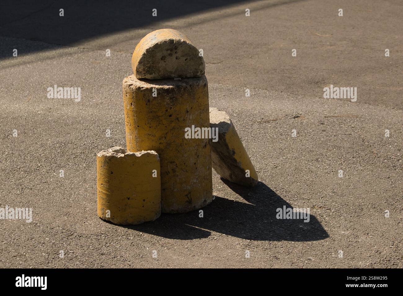Una composizione di barriere di cemento gialle rotte poste su una superficie asfaltata, creando una scena urbana astratta con ombre e texture. Foto Stock
