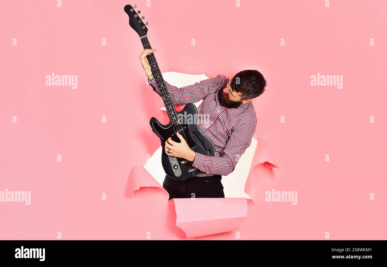 Chitarrista. Uomo barbuto con chitarra elettrica attraverso un foro di carta. Chitarrista rock star con chitarra elettrica. Hobby, strumenti musicali e intrattenimento Foto Stock