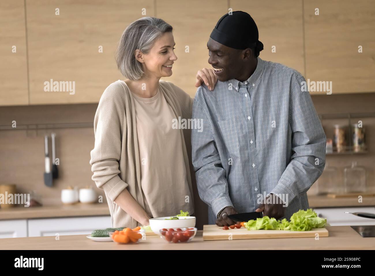 Una coppia multietnica di mezza età felice prepara l'insalata nella cucina di casa Foto Stock