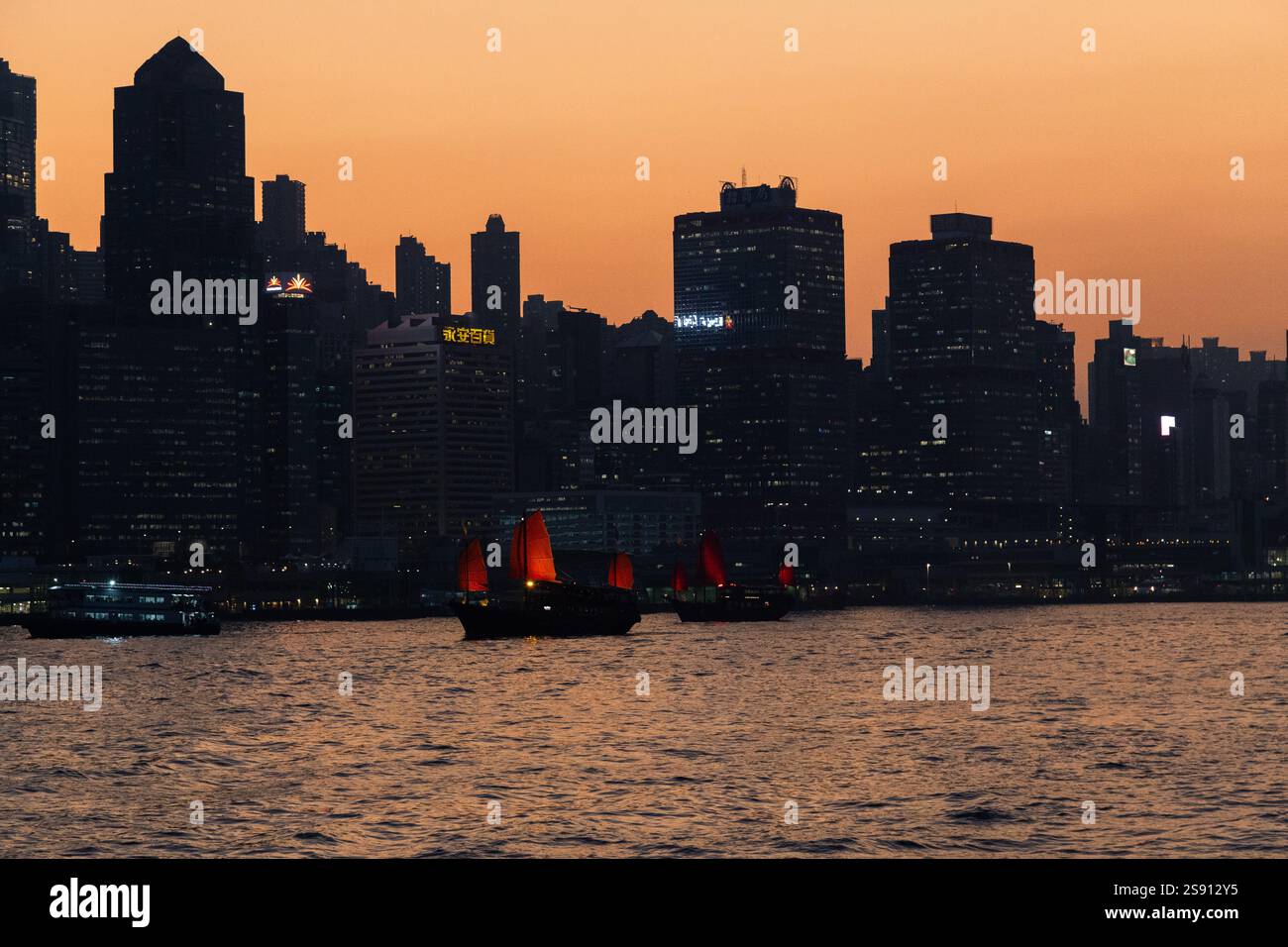 Barche cinesi spazzatura che navigano di notte con lo skyline di Hong Kong Foto Stock