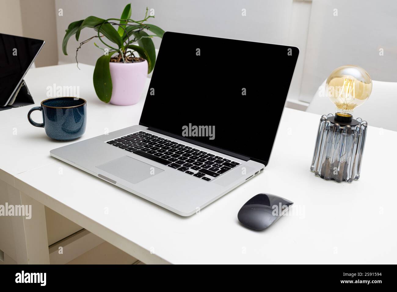 Area di lavoro con laptop, mouse, lampada, tazza da caffè e orchidea Foto Stock