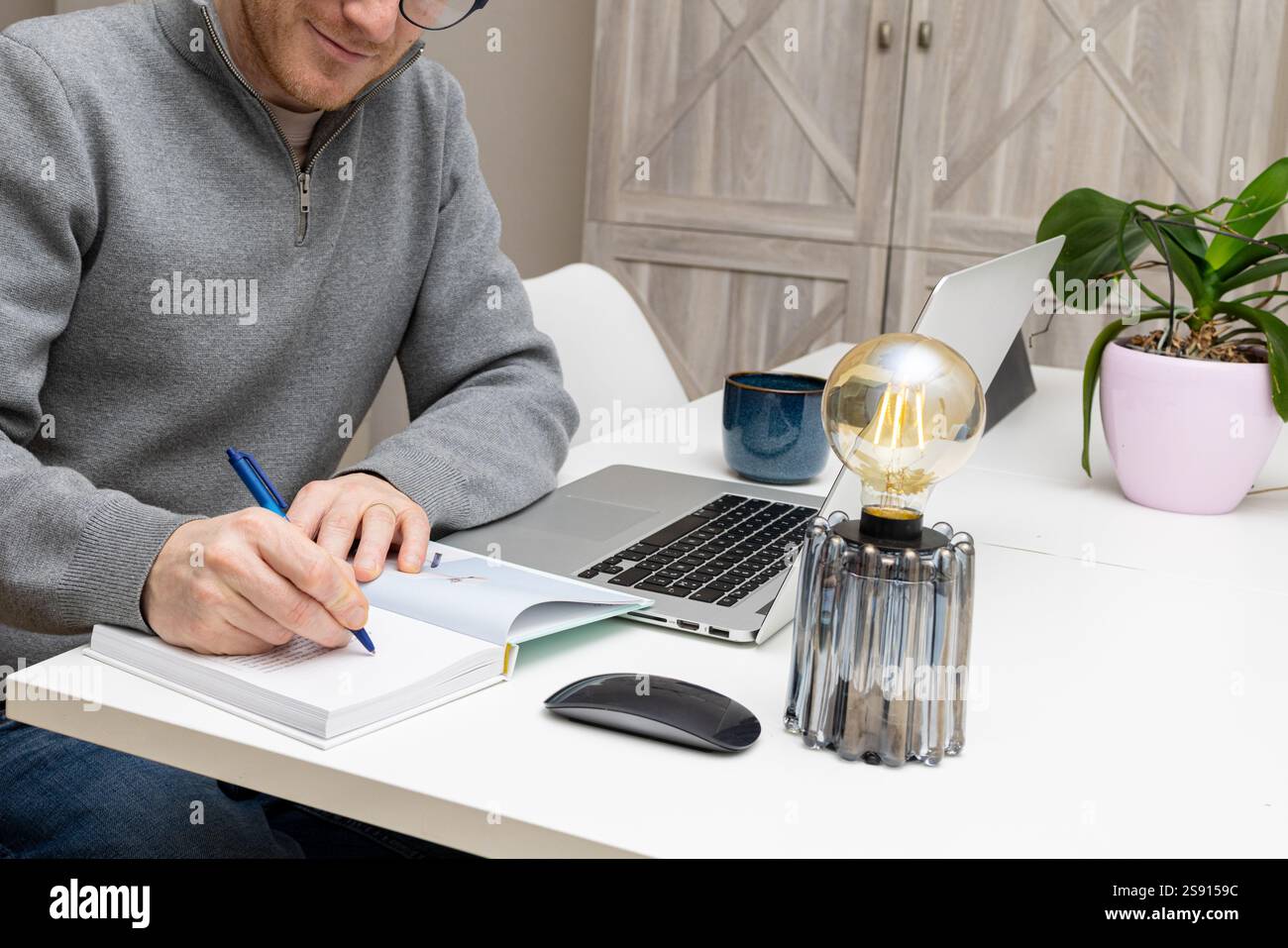 un uomo d'affari sorridente che scrive nel suo libro nel suo ufficio domestico Foto Stock