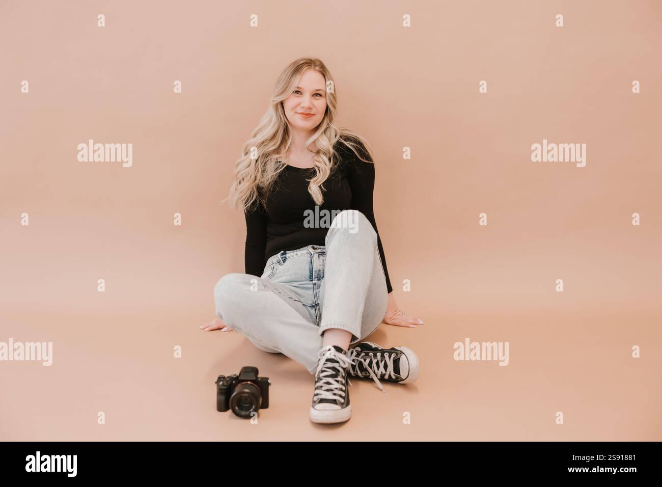 Giovane fotografa seduta con una fotocamera su sfondo beige Foto Stock