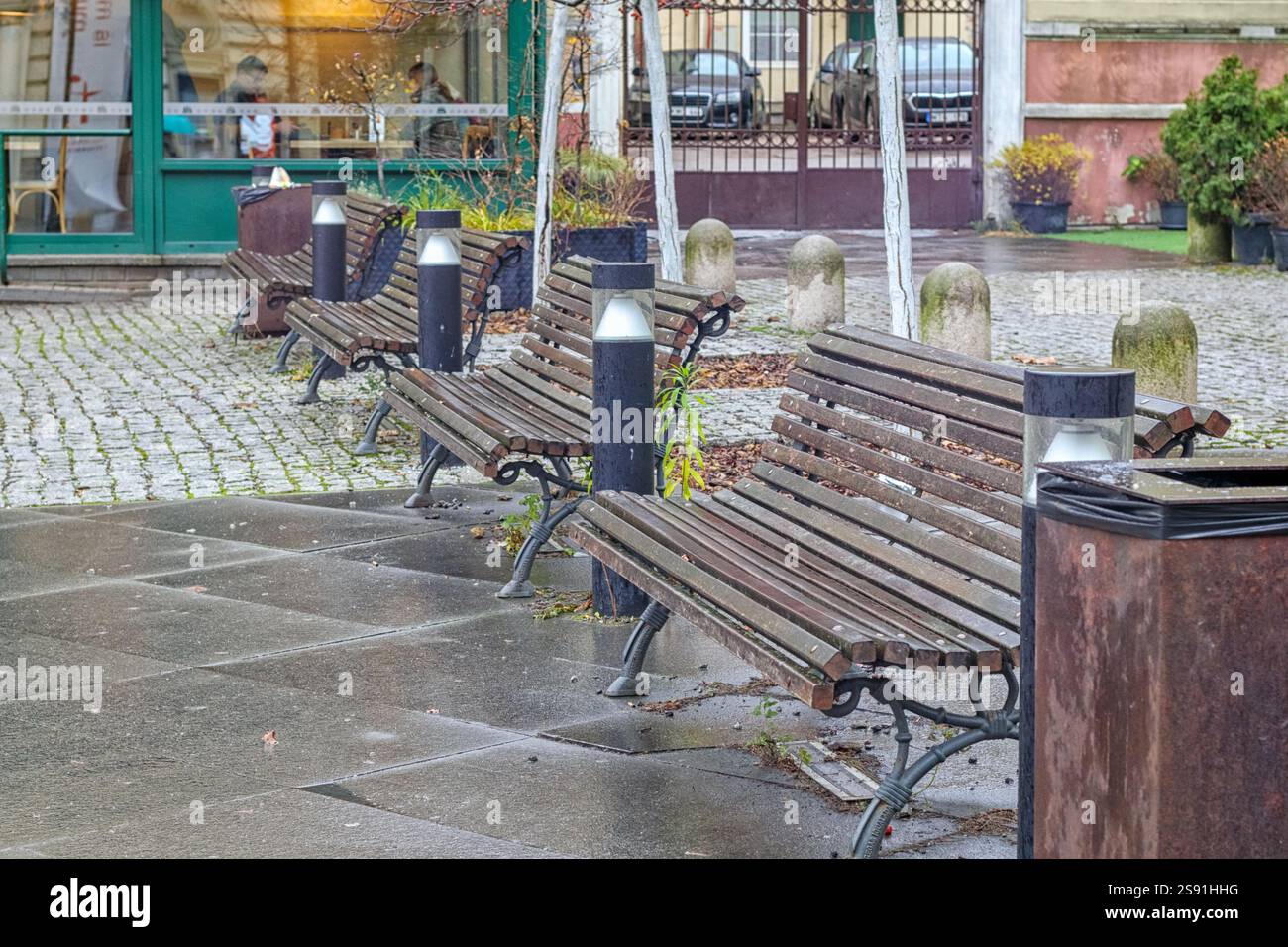 Una piazza vuota con diverse panchine di legno allineate lungo un marciapiede lastricato. Foto Stock
