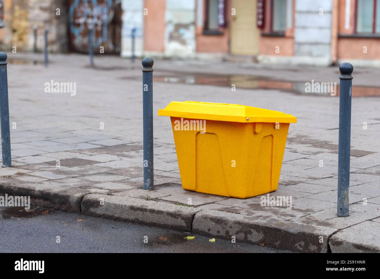 Un grande contenitore per la spazzatura dipinto di giallo posto sul marciapiede di fronte alla casa. Foto Stock