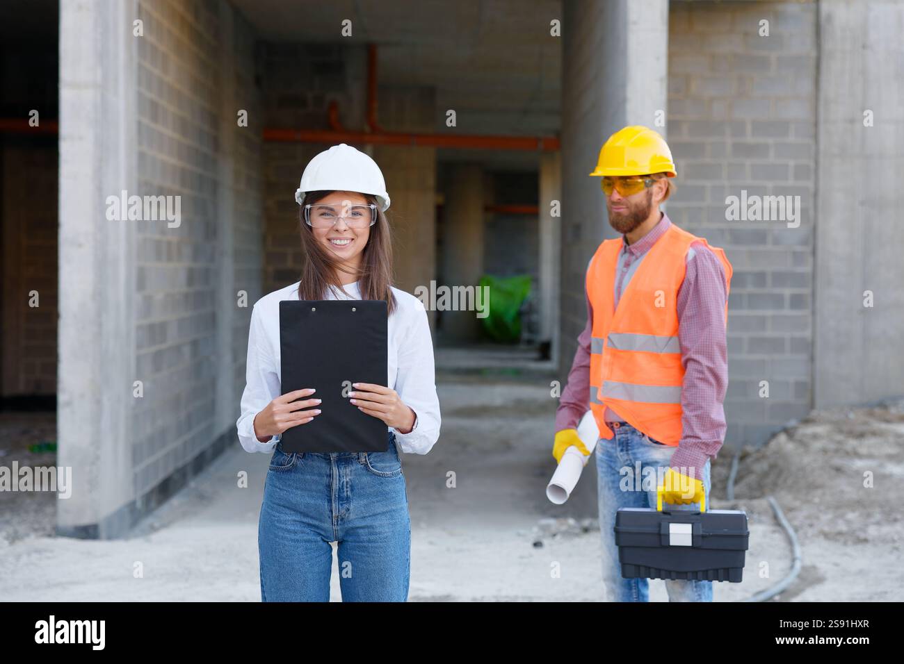 Team di costruzione diversificato in attrezzature di sicurezza che discutono del progetto nel cantiere. La collaborazione e il lavoro di squadra sono evidenti mentre pianificano un nuovo sviluppo Foto Stock