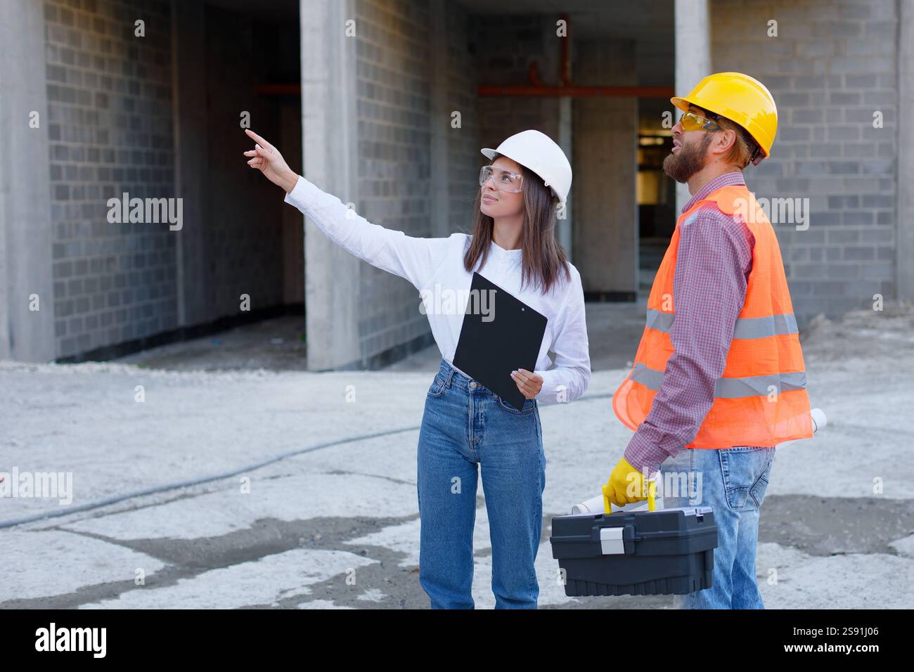 Architetto e operaio edile che indossano caschi di sicurezza e discutono i dettagli del progetto di costruzione in cantiere Foto Stock