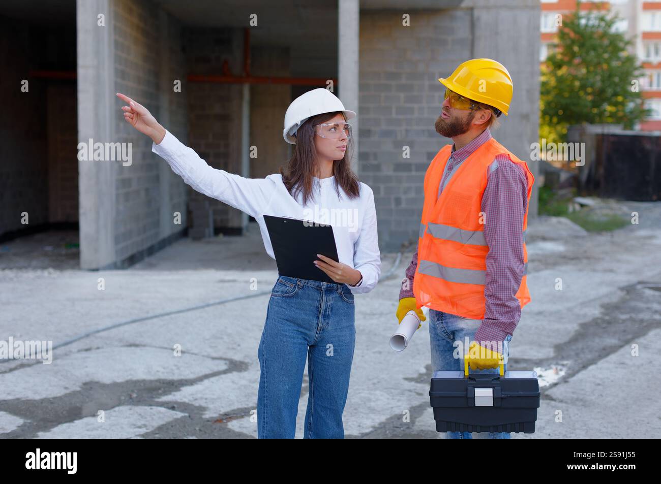 Architetto e operaio edile che indossano caschi di sicurezza e discutono i dettagli del progetto di costruzione in cantiere Foto Stock