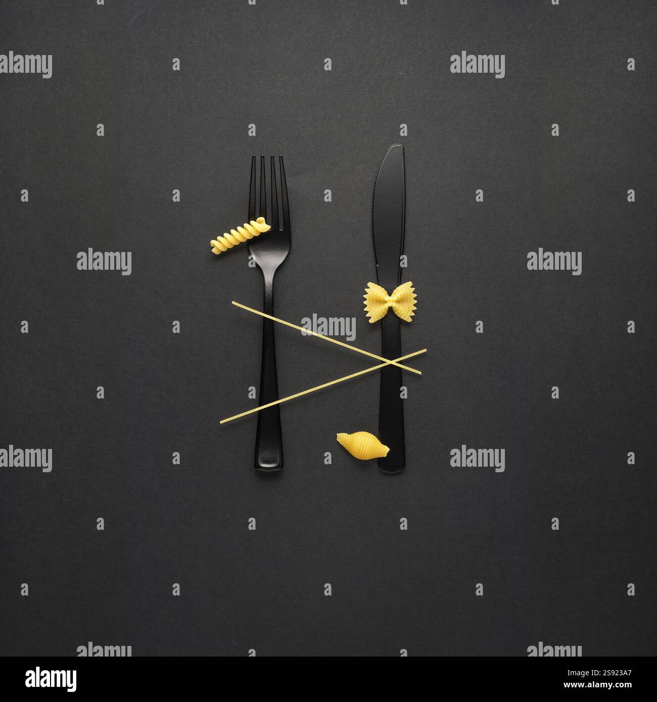 Foto creative di STILL Life con forchetta e cucchiaio con pasta cruda su sfondo nero Foto Stock