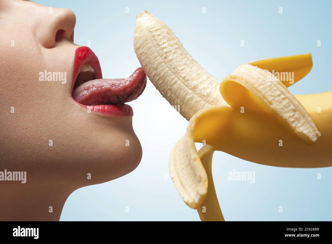 Il volto di una ragazza bollente che lecca una banana gialla mezza pelata Foto Stock