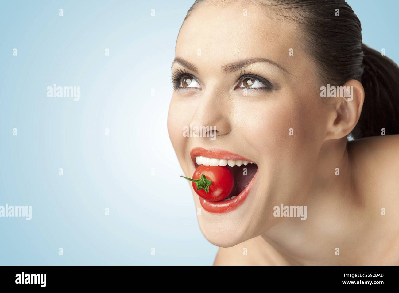 Un ritratto creativo di una bella ragazza che tiene un pomodoro ciliegia tra i denti Foto Stock