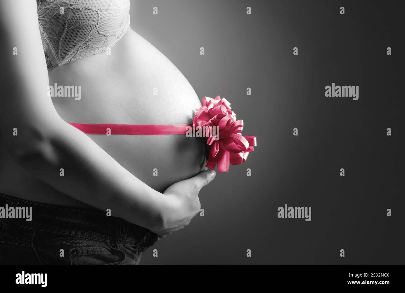 Donna incinta che accarezza la pancia su uno sfondo grigio Foto Stock