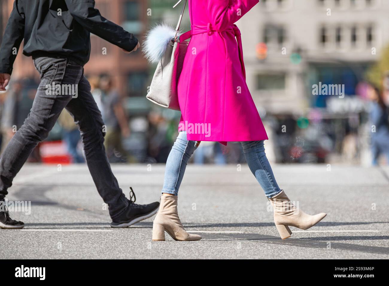 una giovane donna che indossa un cappotto rosa attraversa la strada Foto Stock
