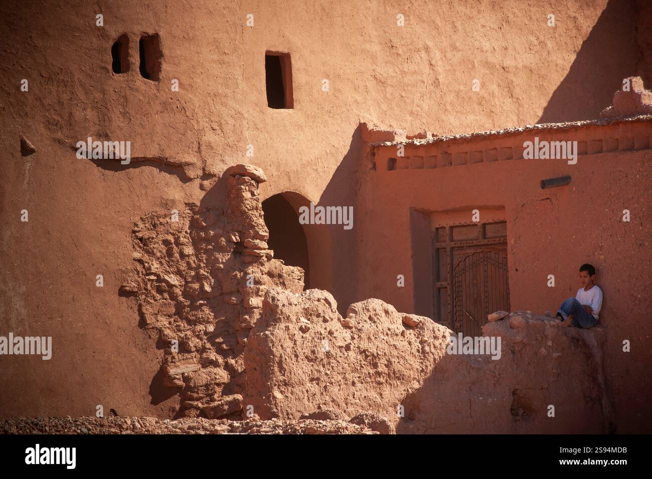 Il ragazzo siede su un muro di argilla fuori dalla Kasbah di Ait Benhaddou, in Marocco Foto Stock