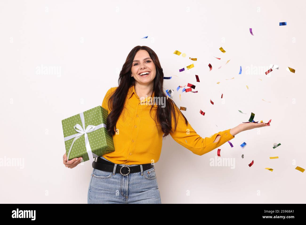 Donna felice con confezione regalo e coriandoli volanti su sfondo bianco. Festa a sorpresa Foto Stock