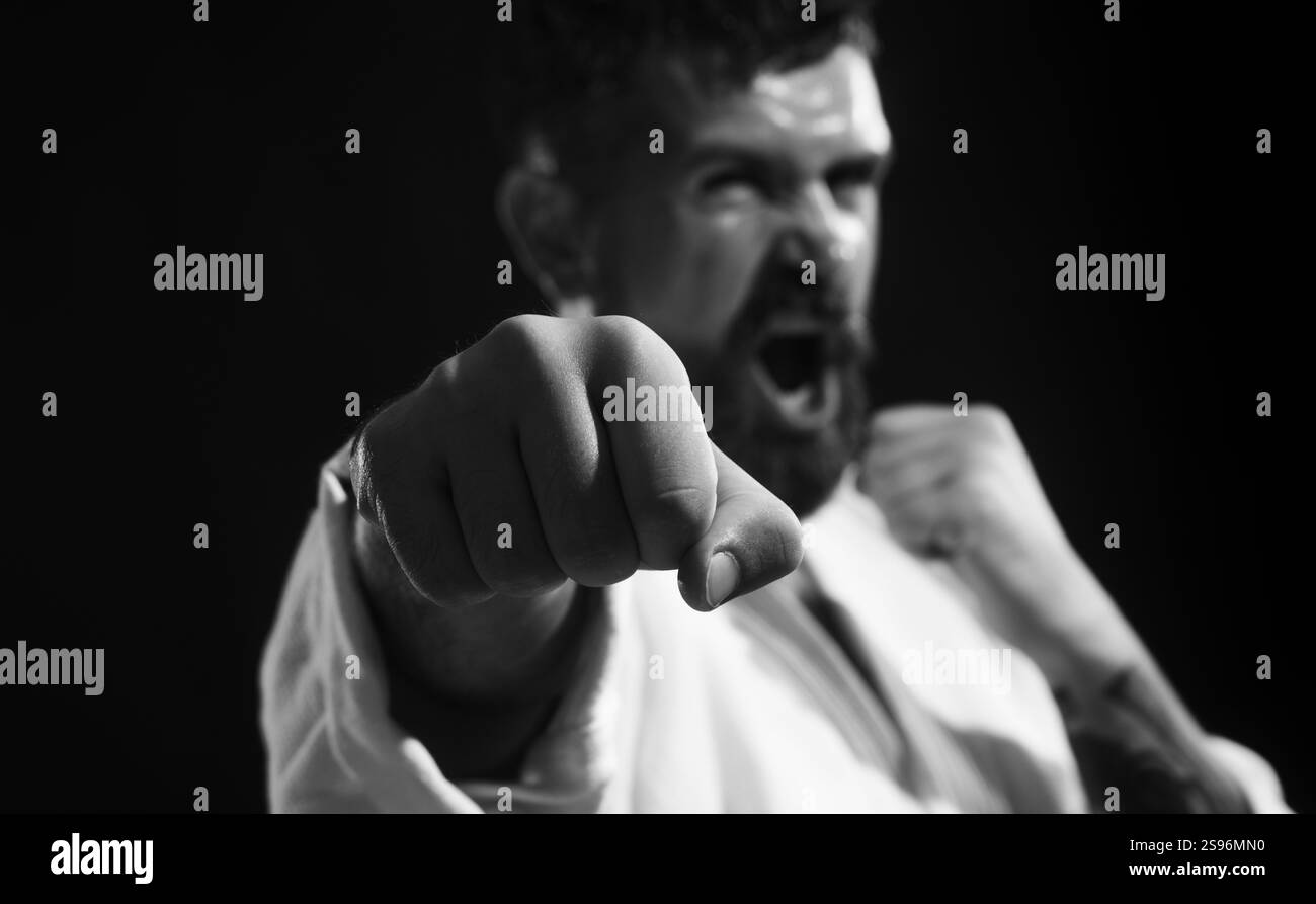 Uomo di karate in posizione di combattimento. Lottatore di karate che pratica il pugno in palestra, concentrati sul pugno. Concetto di sport e fitness. Uomo barbuto in kimono con la mano Foto Stock