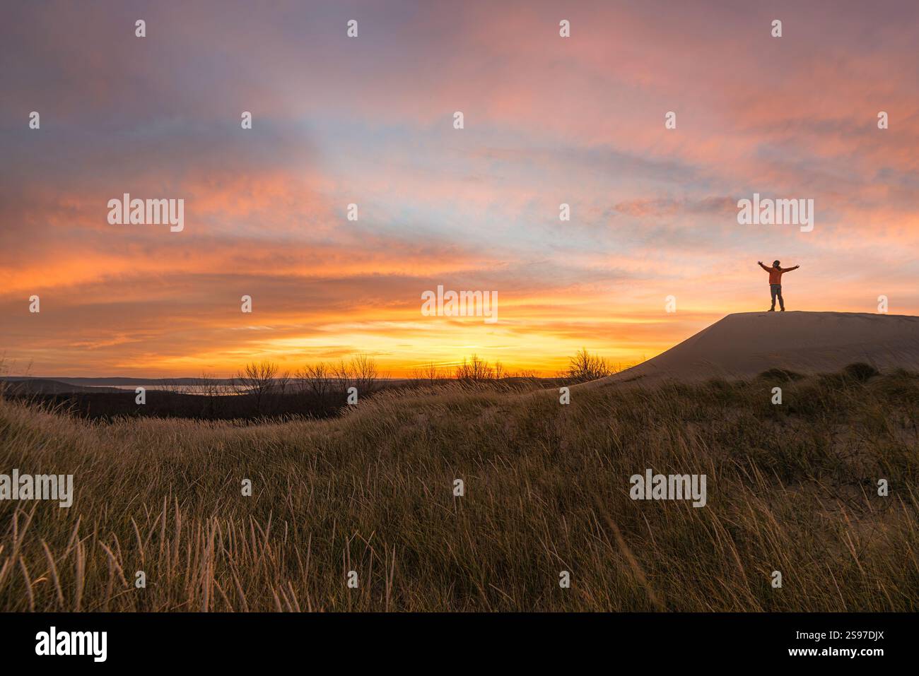 Silhouette di un uomo di mezza età con braccia rialzate che saluta l'alba sul lago Foto Stock