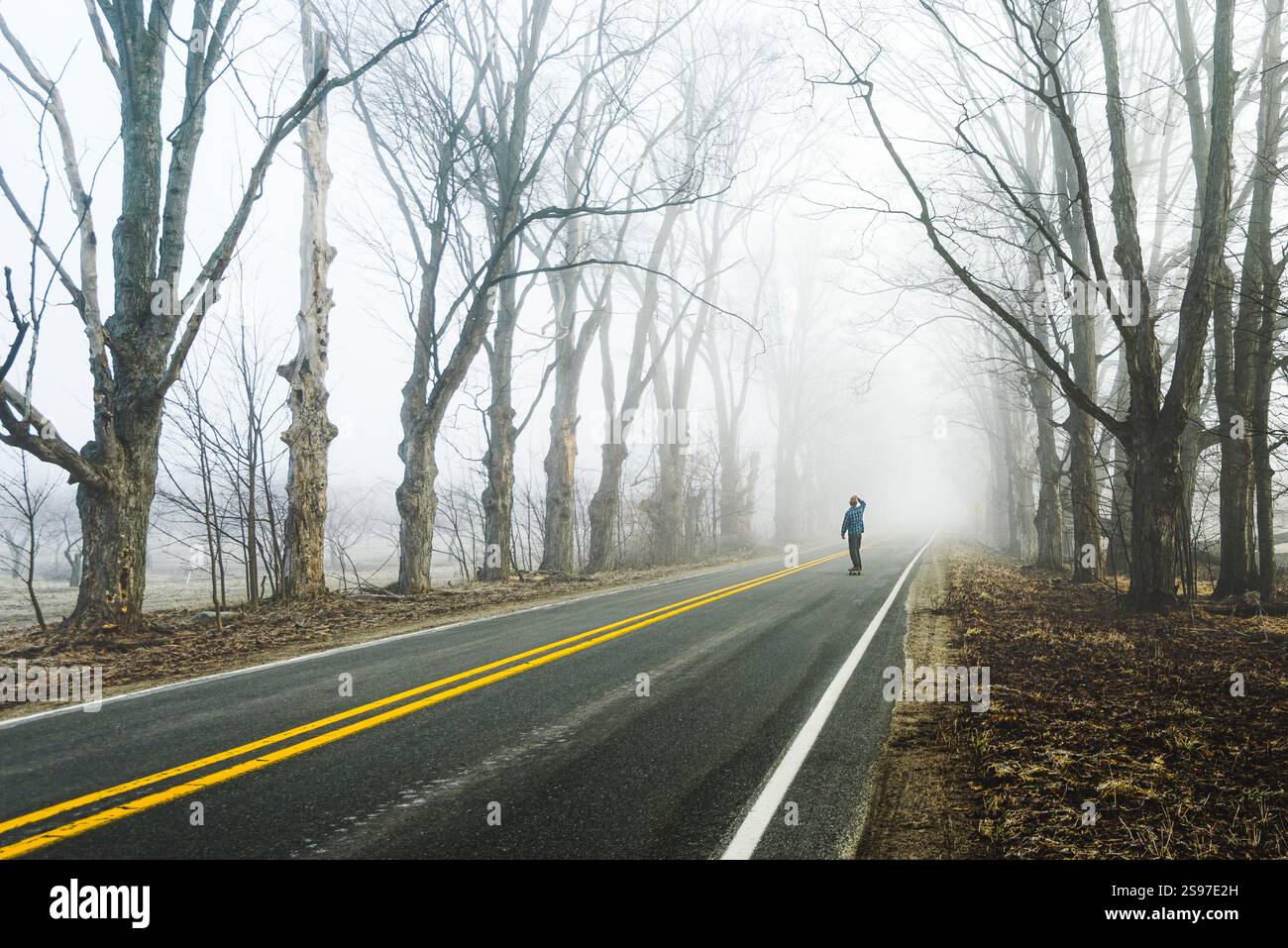 Vista posteriore dello skateboard uomo di mezza età su una strada nebbiosa Foto Stock
