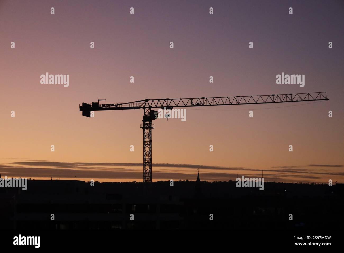 gru da costruzione sagomata contro l'alba dorata (sole, sorgere) sopra lo skyline della città Foto Stock