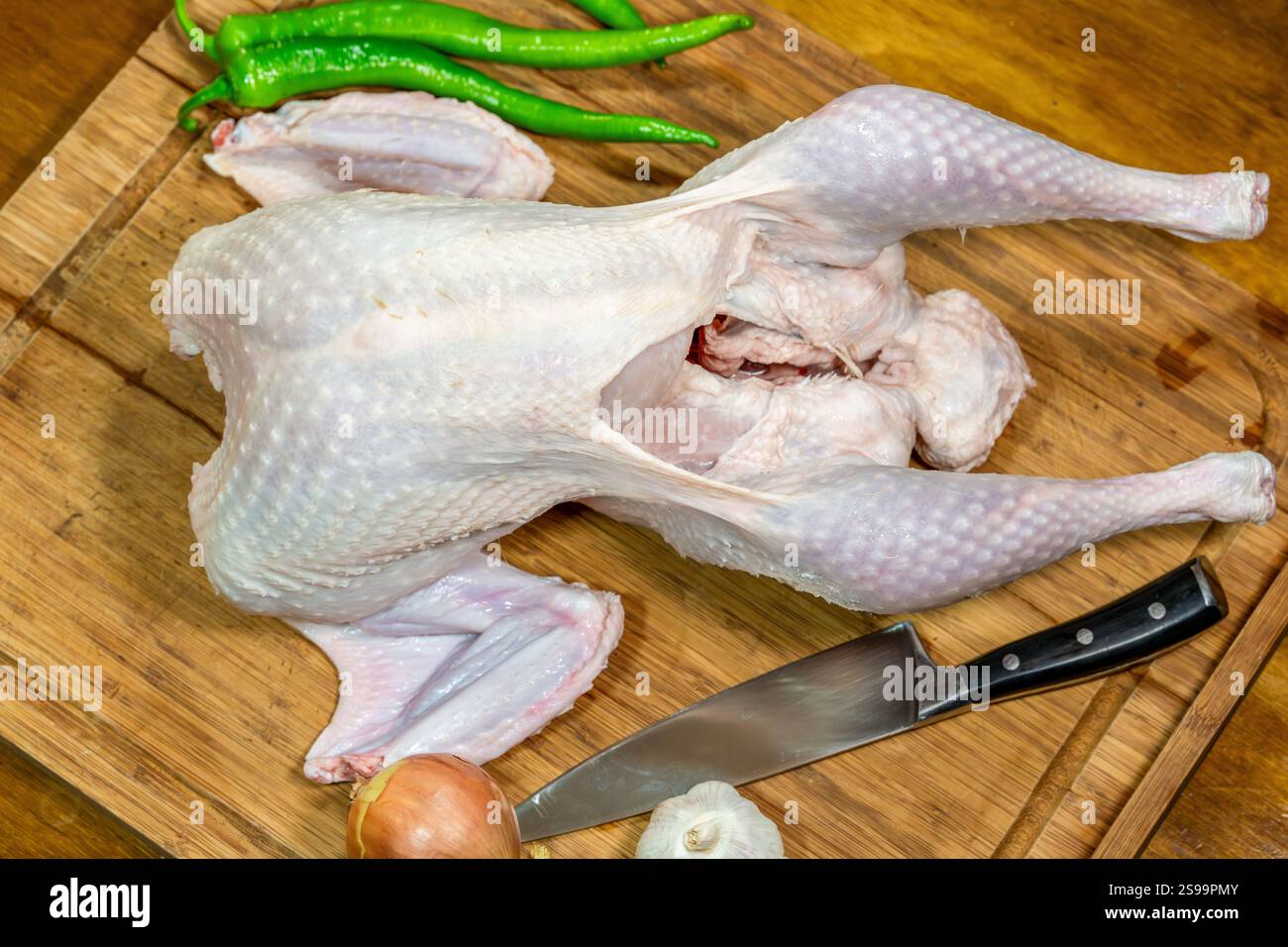 Preparazione di tacchino crudo su tagliere di legno con verdure e coltello Foto Stock