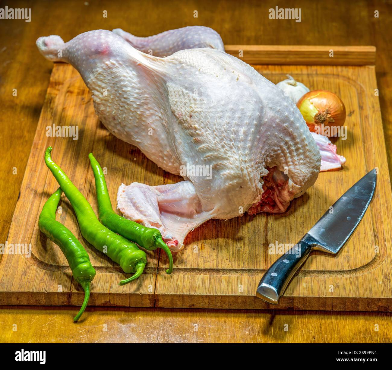 Preparazione di tacchino crudo su tagliere di legno con verdure e coltello Foto Stock