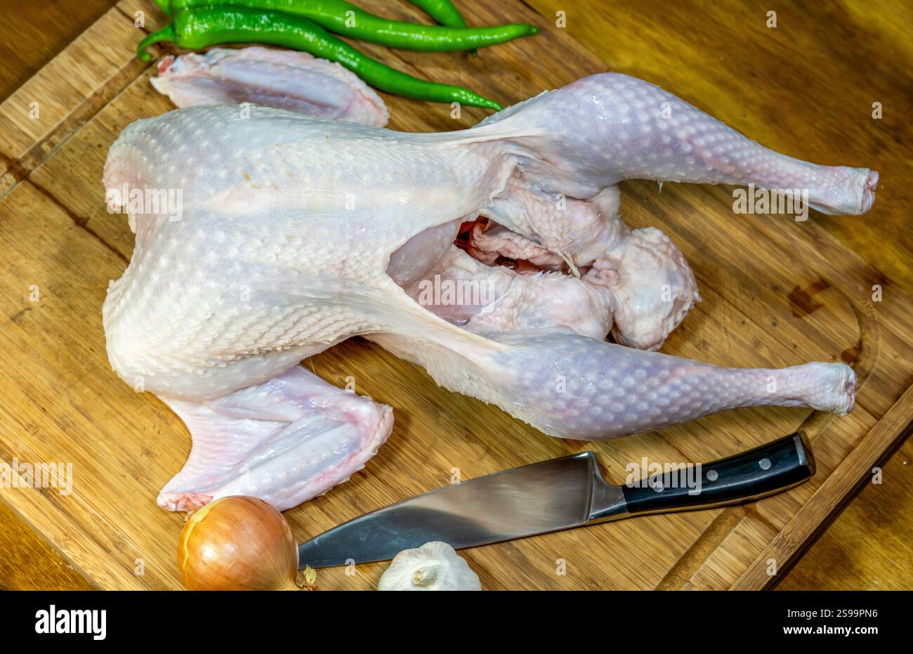 Preparazione di tacchino crudo su tagliere di legno con verdure e coltello Foto Stock
