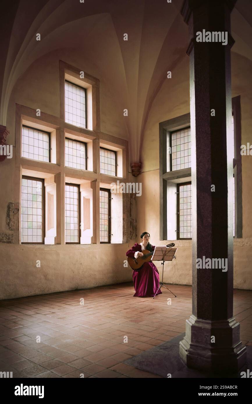 Una donna suona la chitarra mentre è seduta in una grande sala aperta nel castello di Malbrok, Malbork, Polonia, Europa Foto Stock
