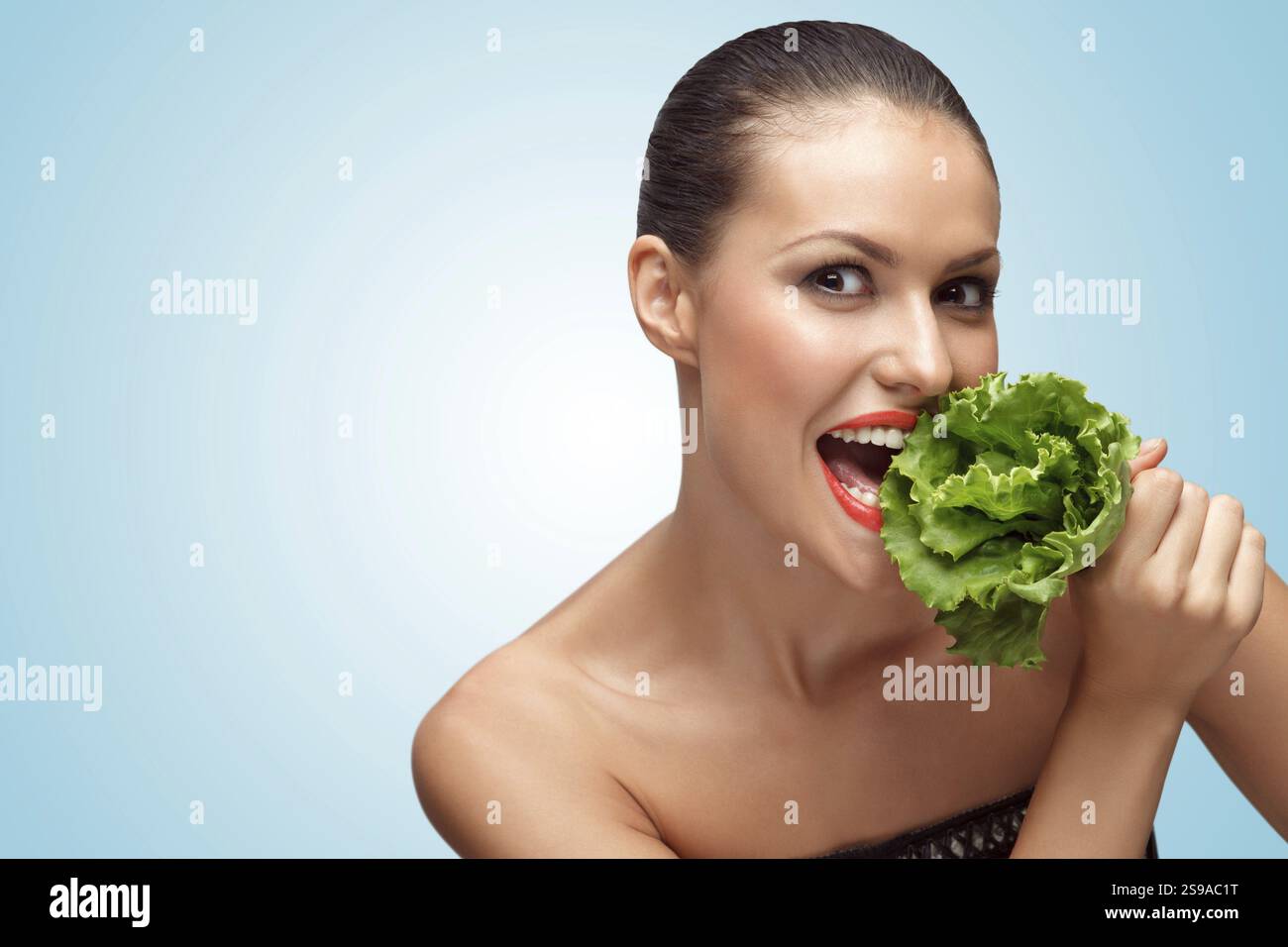 Un ritratto creativo di una bella ragazza affamata a dieta che mangia foglie di insalata verde Foto Stock