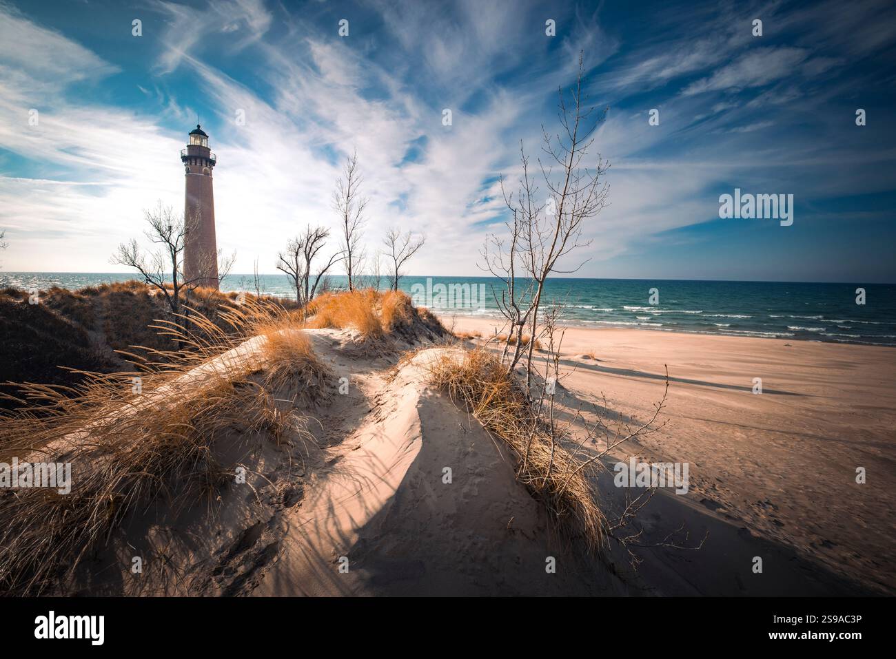 Lo storico faro di Sable si erge alto su una spiaggia di sabbia incontaminata, circondato da dune e affacciato sul vasto e sereno oceano sotto un cielo blu brillante. Foto Stock