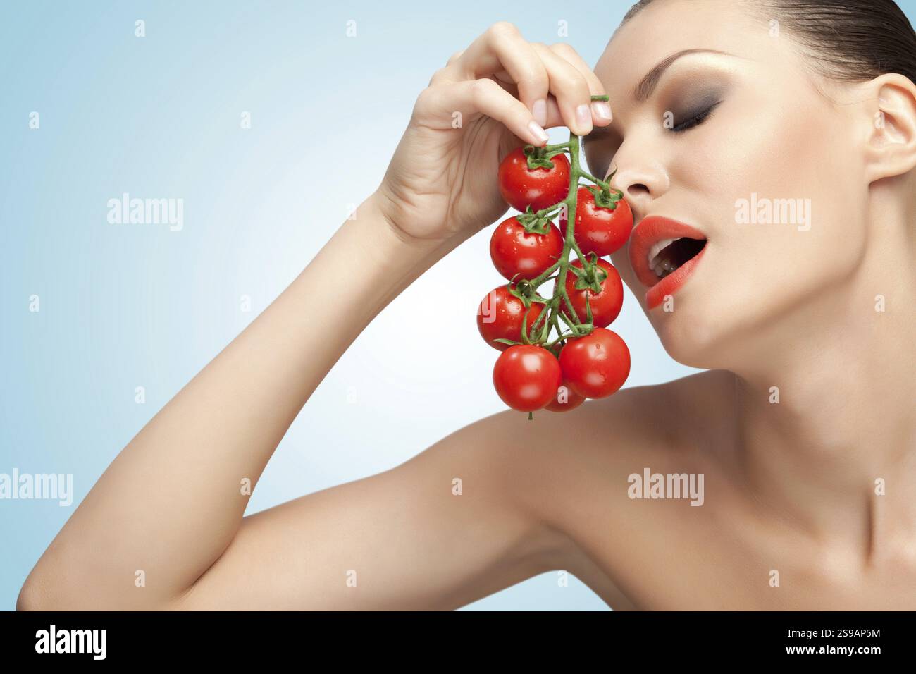 Un ritratto creativo di una bella ragazza che tiene sessualmente un mucchio di pomodori ciliegini vicino alla bocca Foto Stock