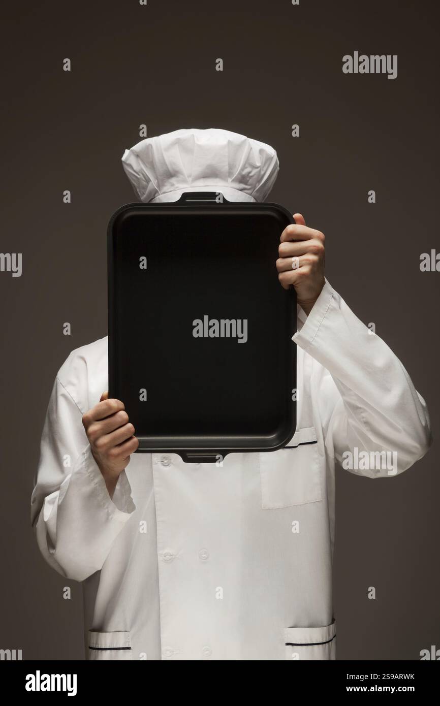 Un ritratto del fornaio nascosto dietro il vassoio da forno Foto Stock